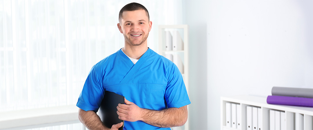 Healthcare worker in blue scrubs holding a tablet.